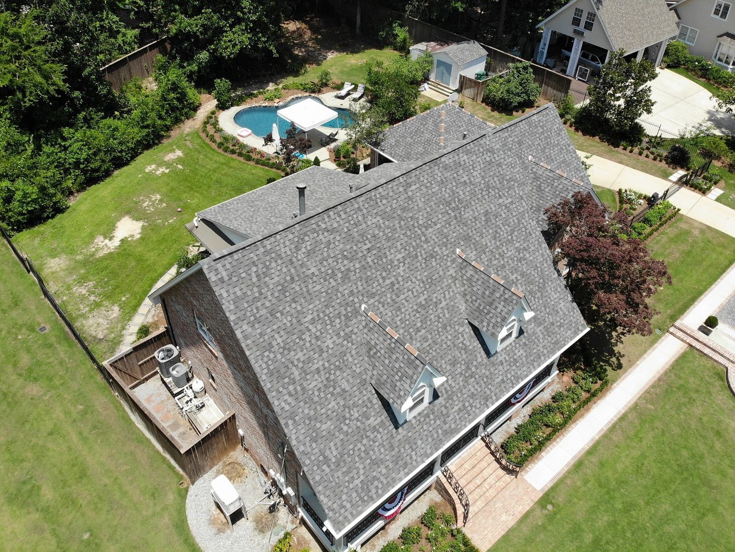 Aerial view of a house with a pool, green lawn, and surrounding trees.
