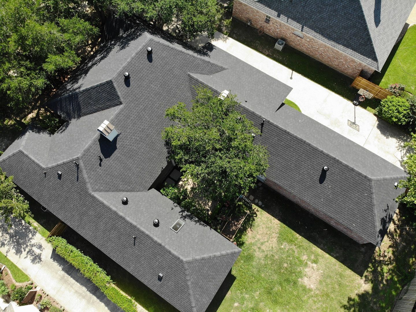 Aerial view of a house with a dark roof surrounded by green grass and trees.