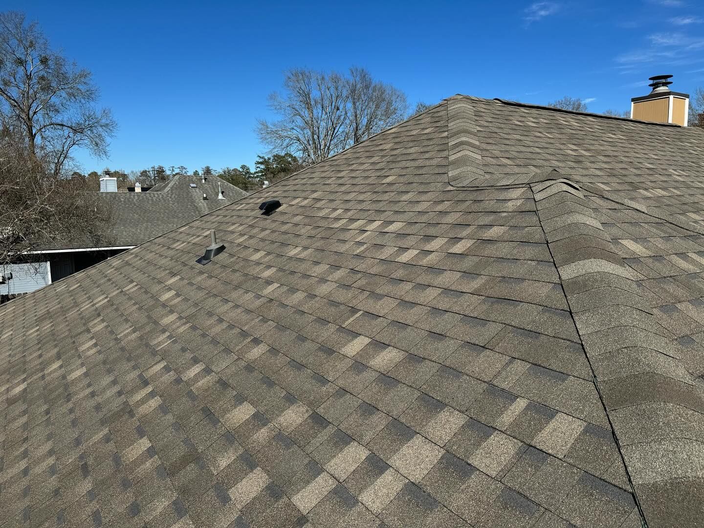 A brown asphalt shingle roof on a house against a clear blue sky.