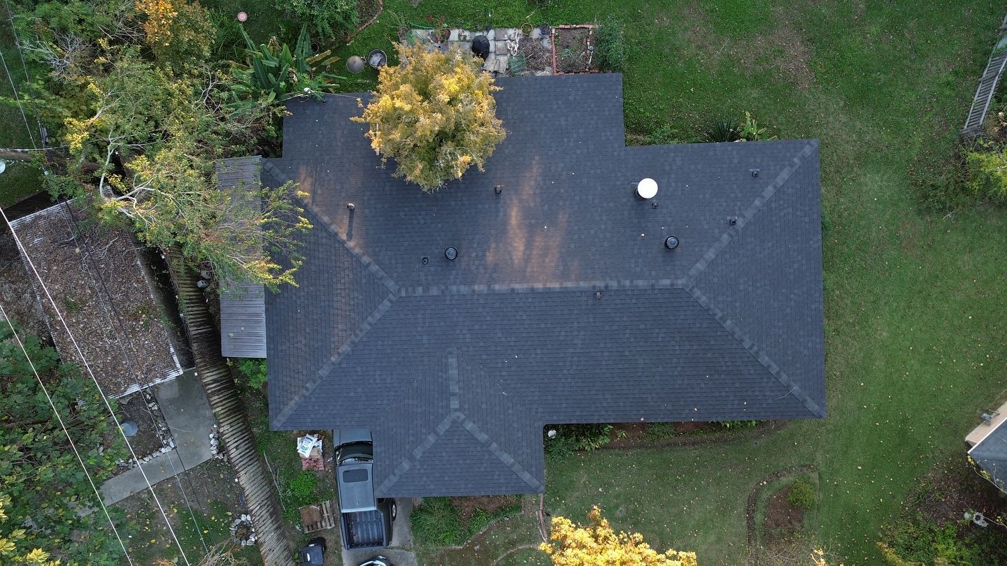 Overhead view of a house with a dark roof, a tree growing through it, and surrounding green grass.
