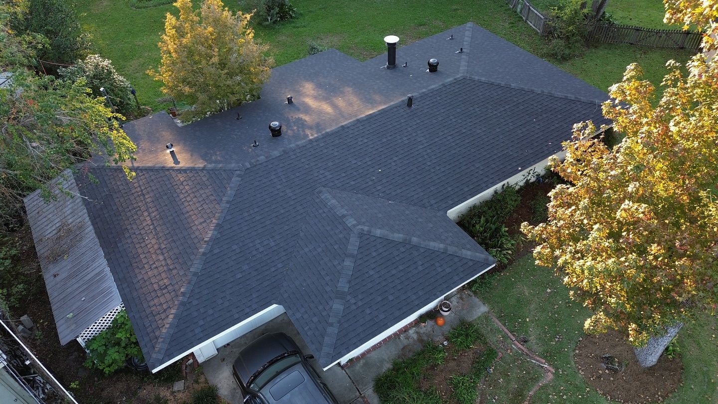 Overhead view of house with dark roof, car in driveway, and trees.