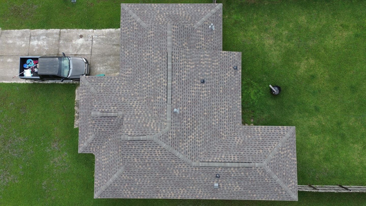 Aerial view of a house with a weathered roof, a pickup truck, and green grass.
