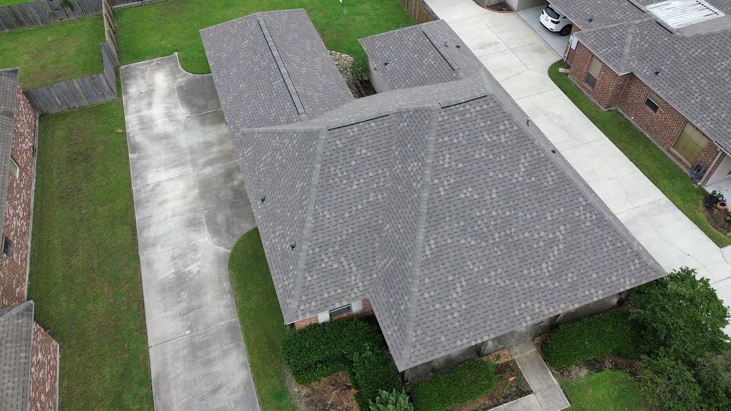 Overhead view of multi-unit residential buildings with gray roofs and driveways surrounded by grass and trees.