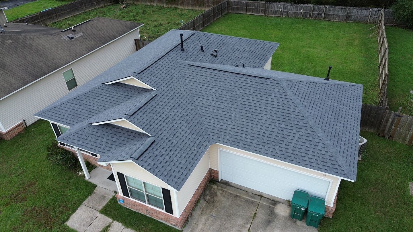 Aerial view of a house with a gray roof, green lawn, and two green trash bins.