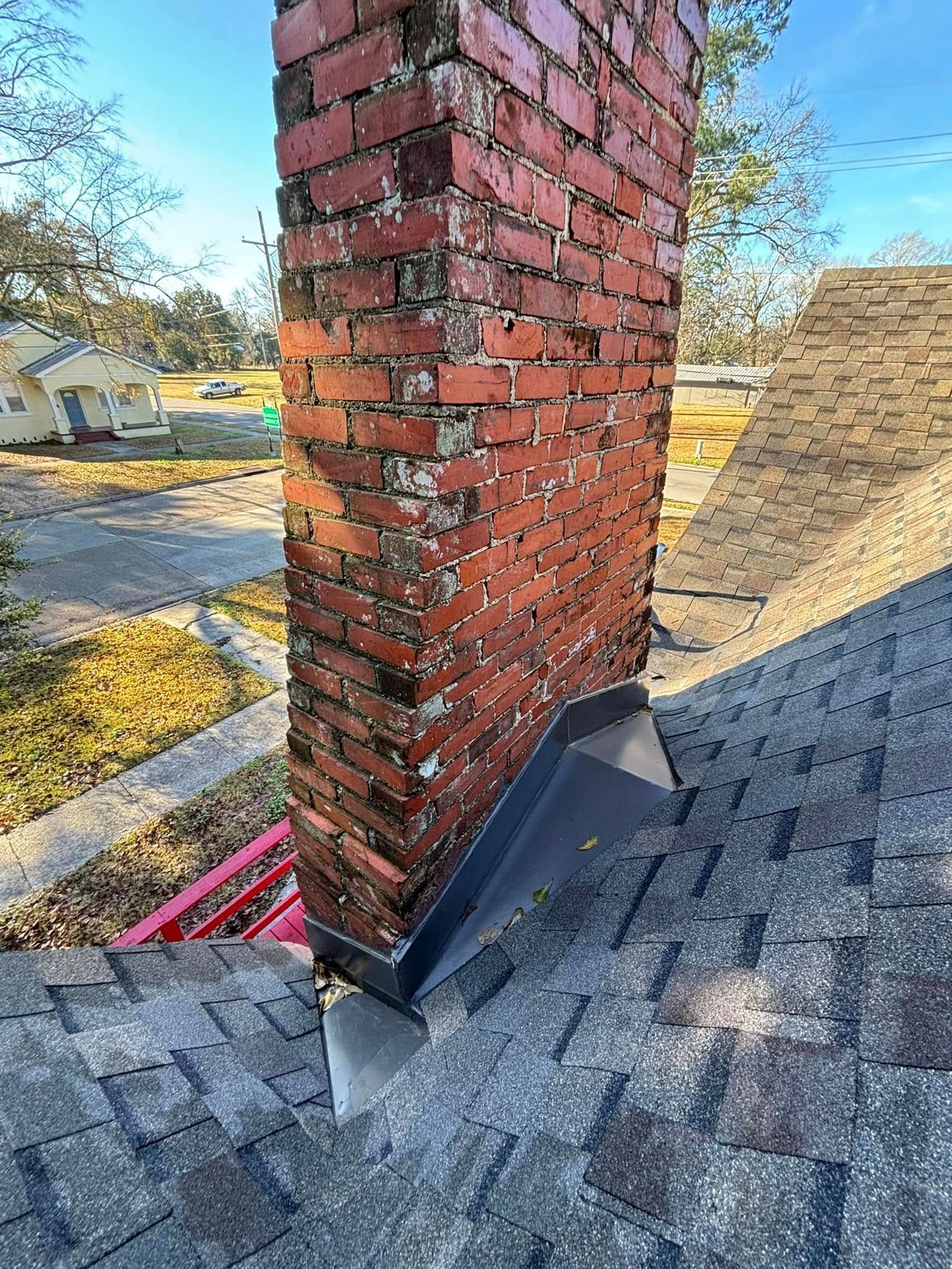 Brick chimney on a roof with weathered shingles and dark metal flashing.