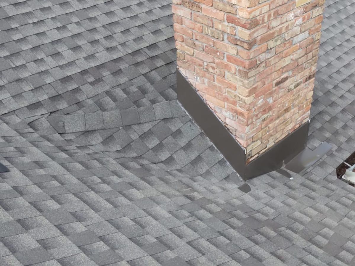 Gray shingled roof with a brick chimney; area of shingle damage is visible near the chimney.
