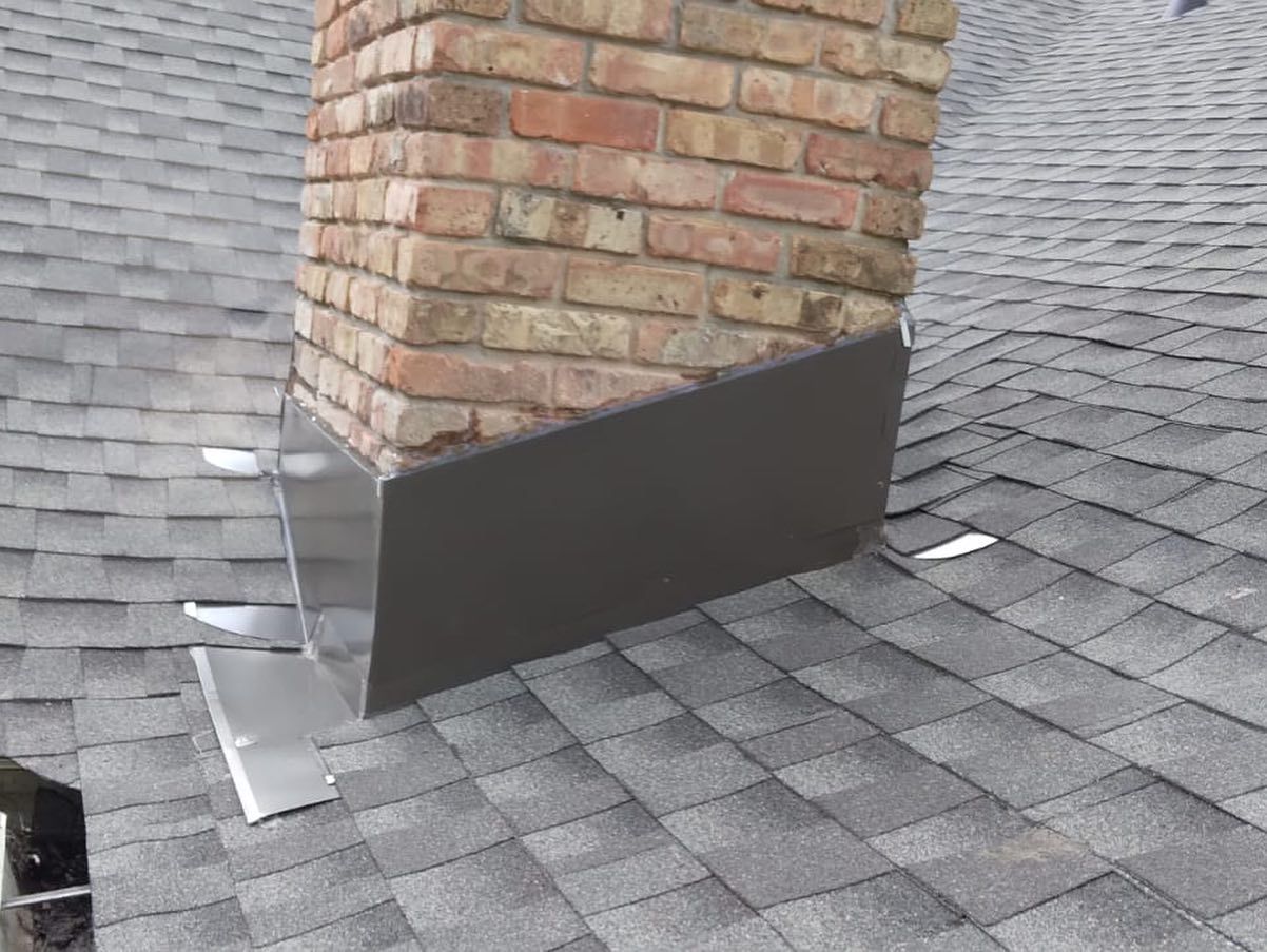 Brick chimney on gray shingle roof with dark metal flashing at the base.