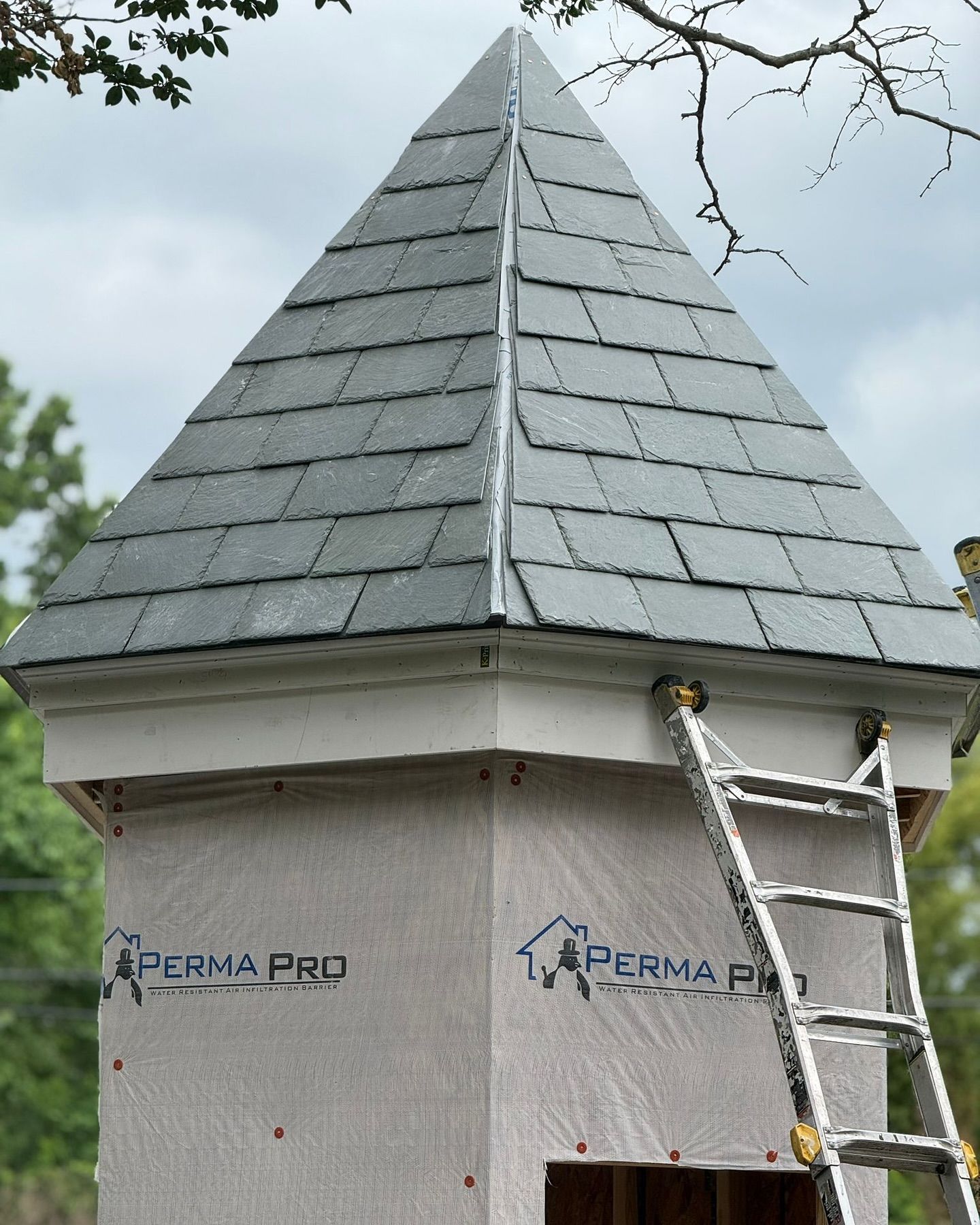 A gray slate roof on a tower under construction with a ladder leaning against it.