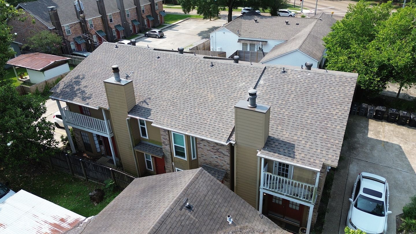 Townhouses with brown shingle roofs, chimneys, balconies, and parked cars. Green trees in the background.