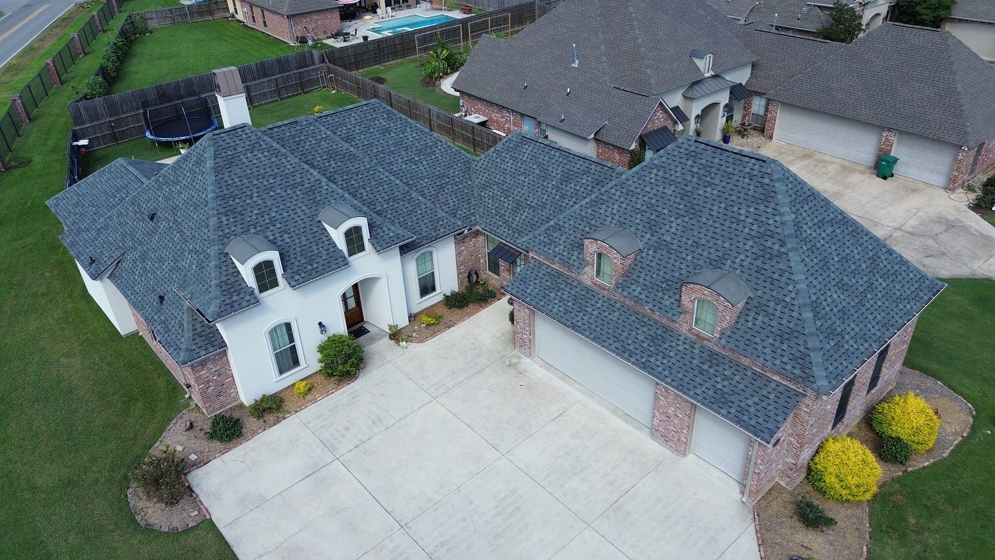 Aerial view of a brick and white house with a gray roof and driveway, surrounded by green grass.