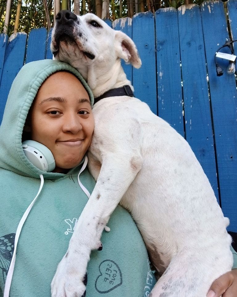 A woman in a green hoodie is holding a white dog