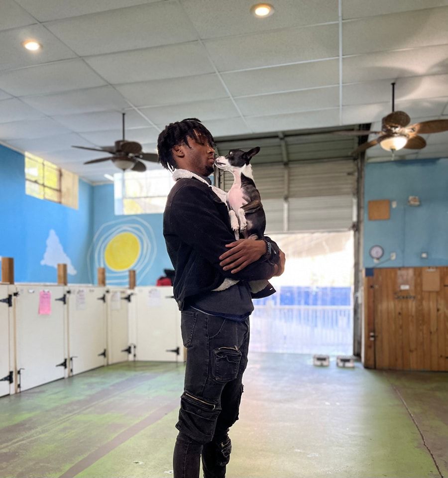 A man is holding a dog in his arms in a room with ceiling fans.