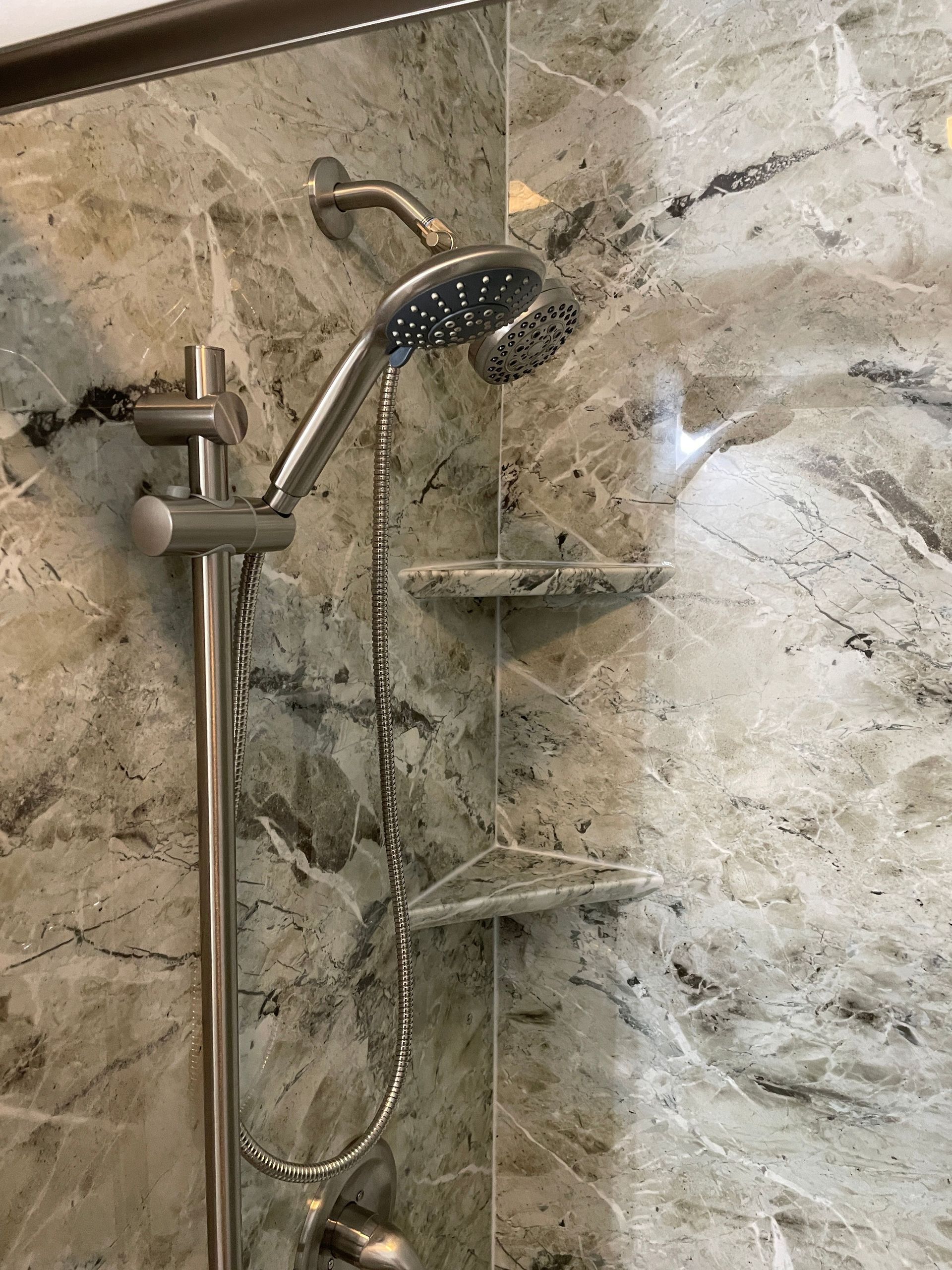 Stainless steel handheld showerhead and hose mounted on a beige stone-tiled shower wall.