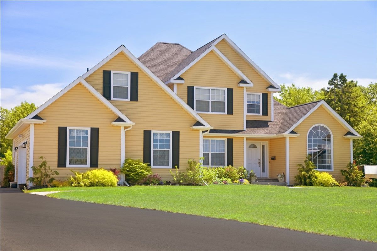 Yellow suburban house with white trim, a green lawn, and a clear blue sky