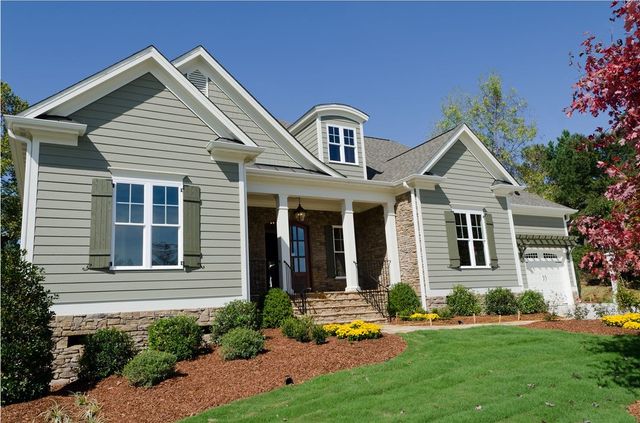 Suburban house with gray siding, white trim, a front porch, and a green lawn in bright daylight