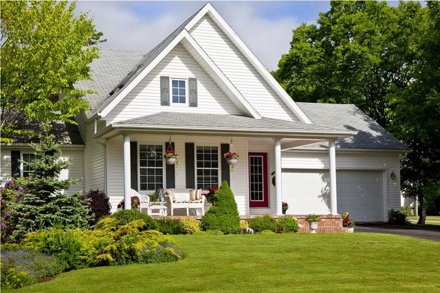 White suburban house with a front porch, red door, garage, and green lawn on a sunny day
