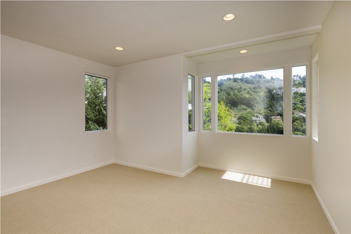 Bright empty room with beige carpet, white walls, and large windows letting in sunlight.
