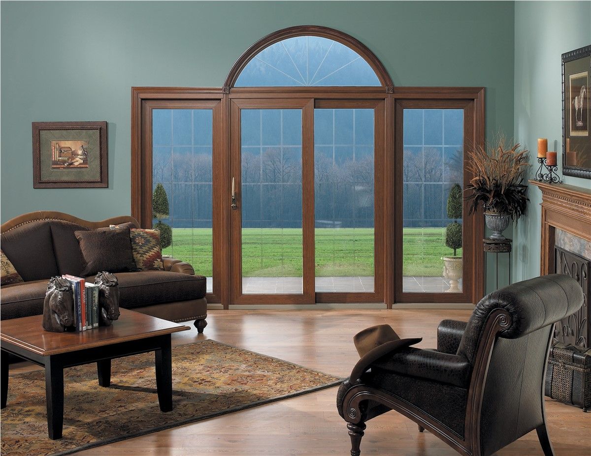 Elegant living room with leather chairs, coffee table, fireplace, and large arched patio doors overlooking a lawn