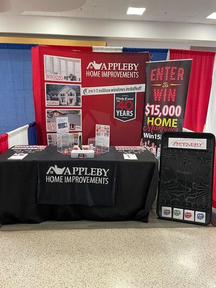 Appleby Home Improvements booth with red signs, black tablecloth, and “Enter to win $15,000 home” display