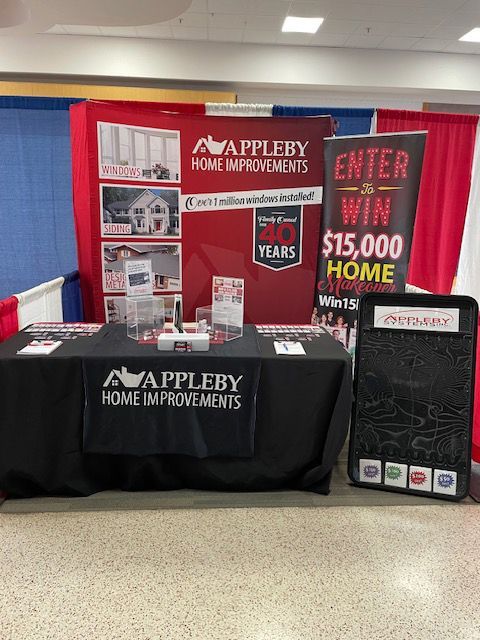 Appleby Home Improvements booth with red signs, black tablecloth, and &ldquo;Enter to win $15,000 home&rdquo; display