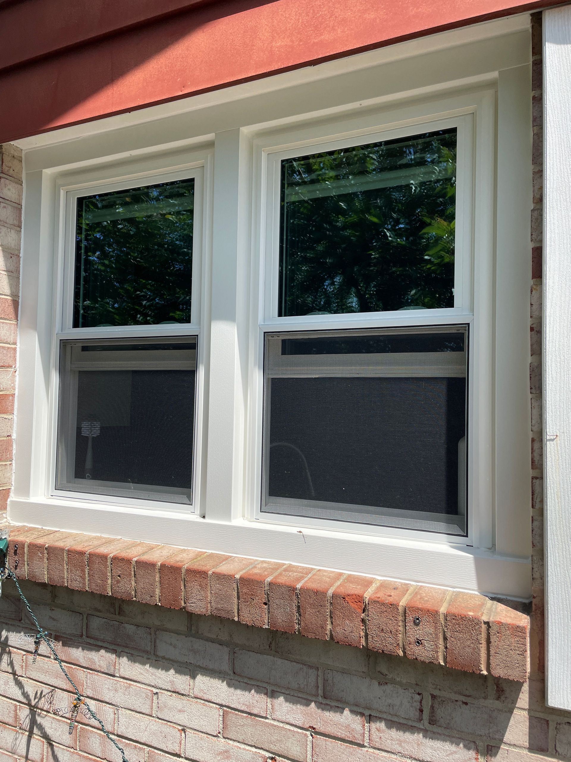 White-framed double window on a brick house exterior with a red roof overhang.
