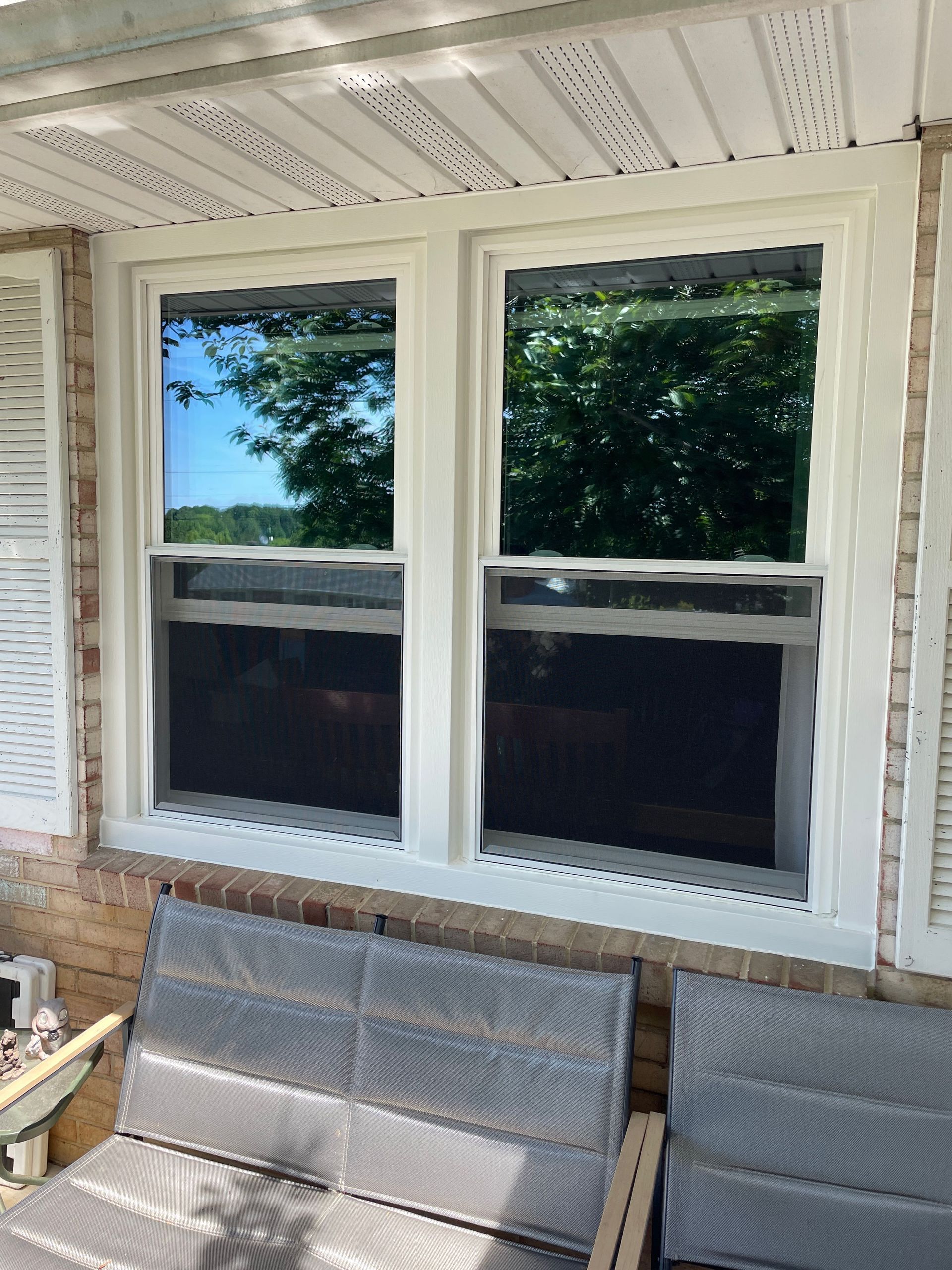 Porch window with white trim and two dark screens above wicker seating, reflecting trees outside