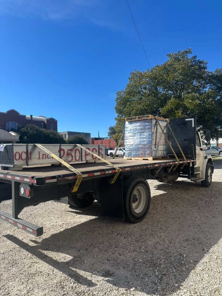 A flatbed truck carrying a pallet of bricks and a few metal sheets on a sunny day.