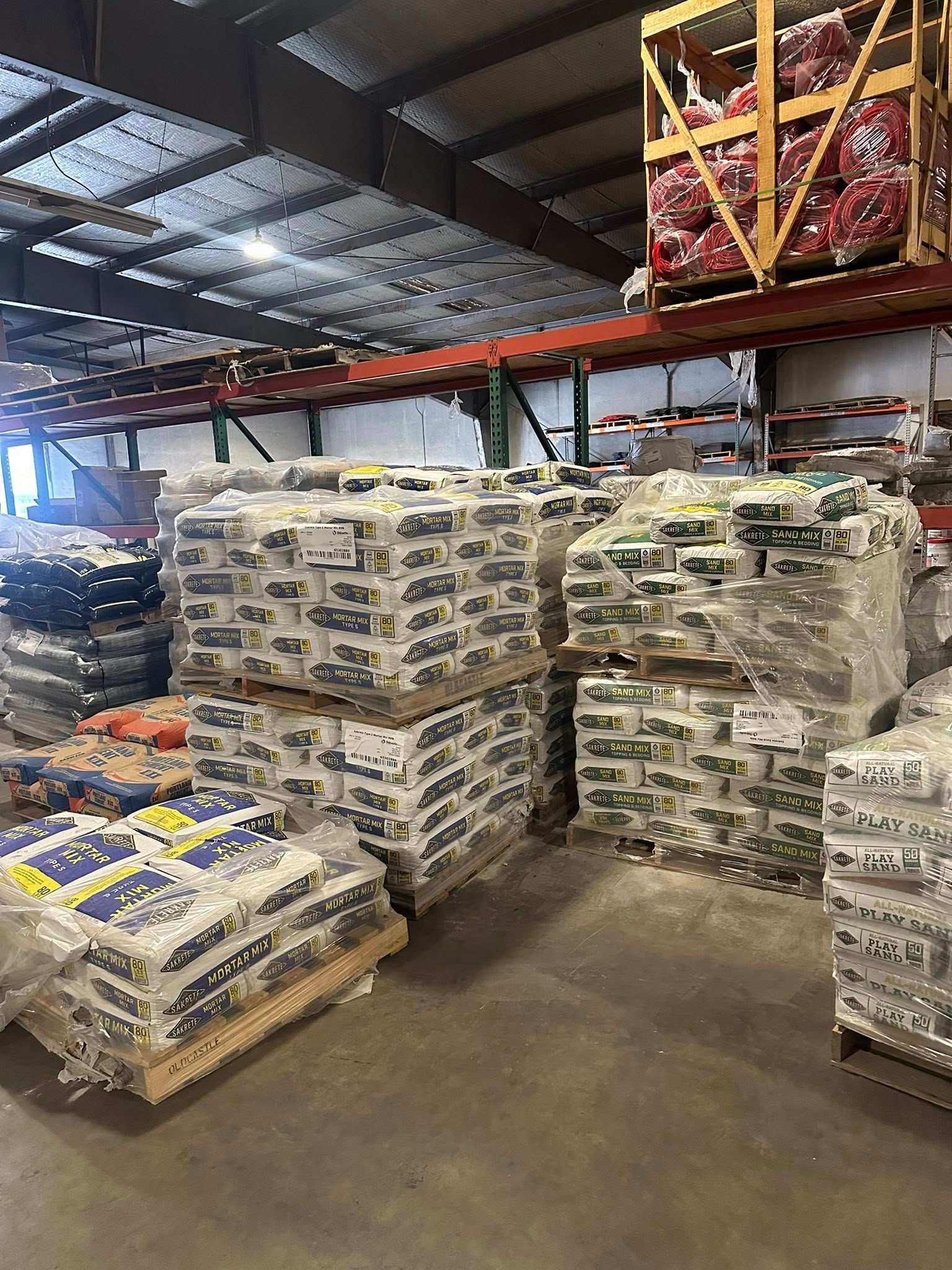Warehouse interior with pallets of bagged products, shelves, and a large overhead storage structure.