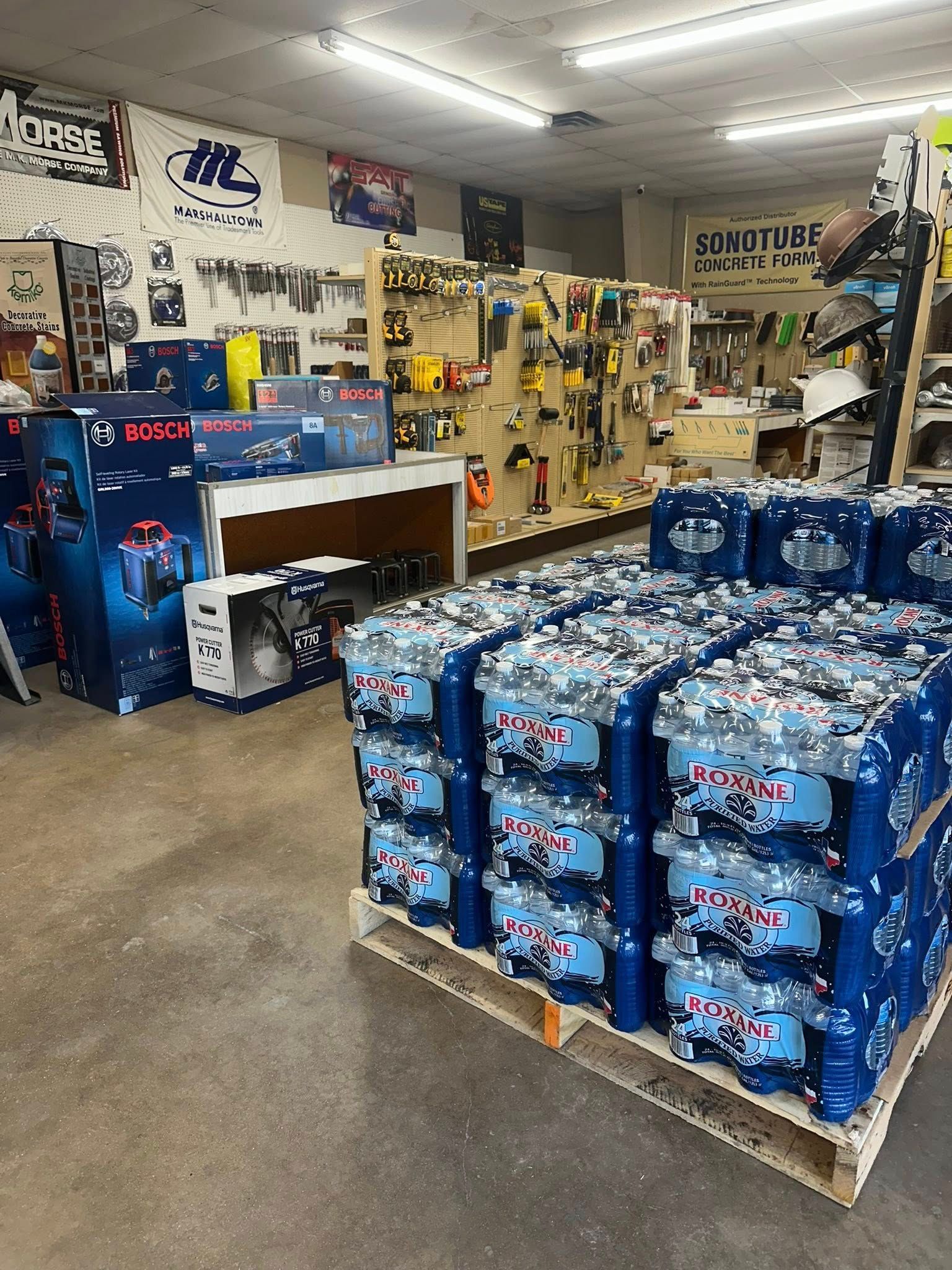 Interior of a store, shelves stocked with tools and equipment, pallets of bottled water in the foreground.