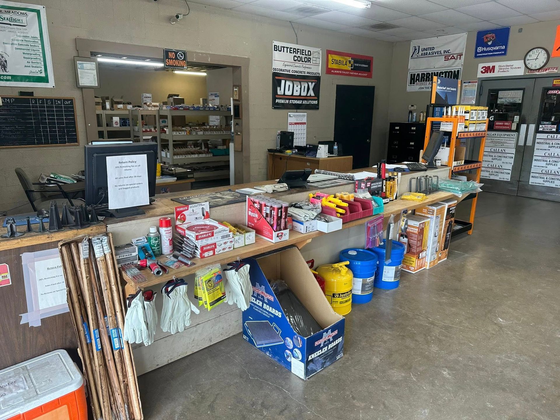 Inside view of a hardware store's counter, stocked with various items. Shelves and doors are visible.