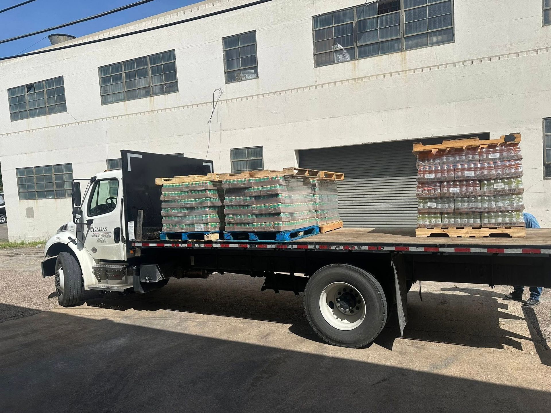 Truck carrying multiple pallets of glass bottles in front of a white building.