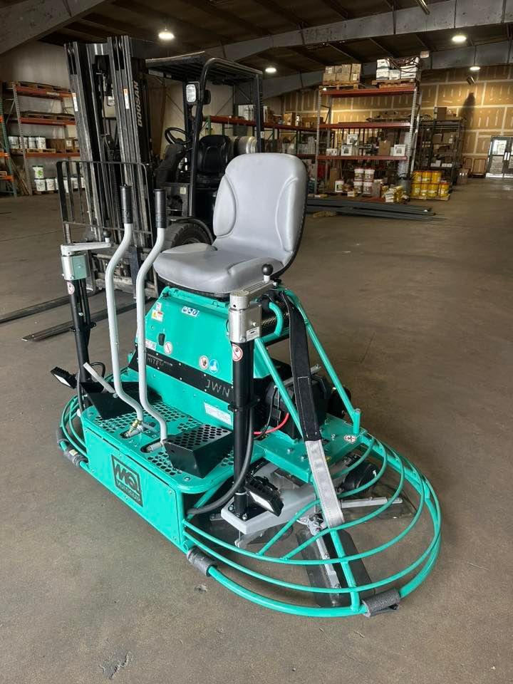 A teal concrete finishing machine with a seat, inside a warehouse.