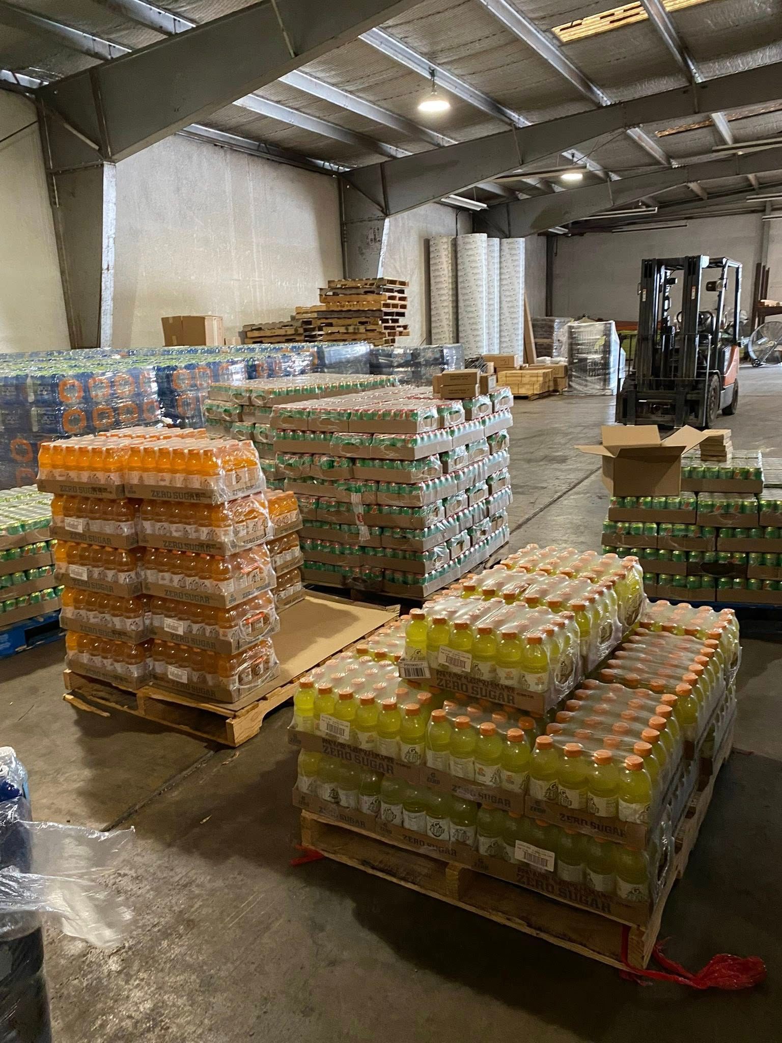 Warehouse interior with pallets of packaged drinks, a forklift in the background.