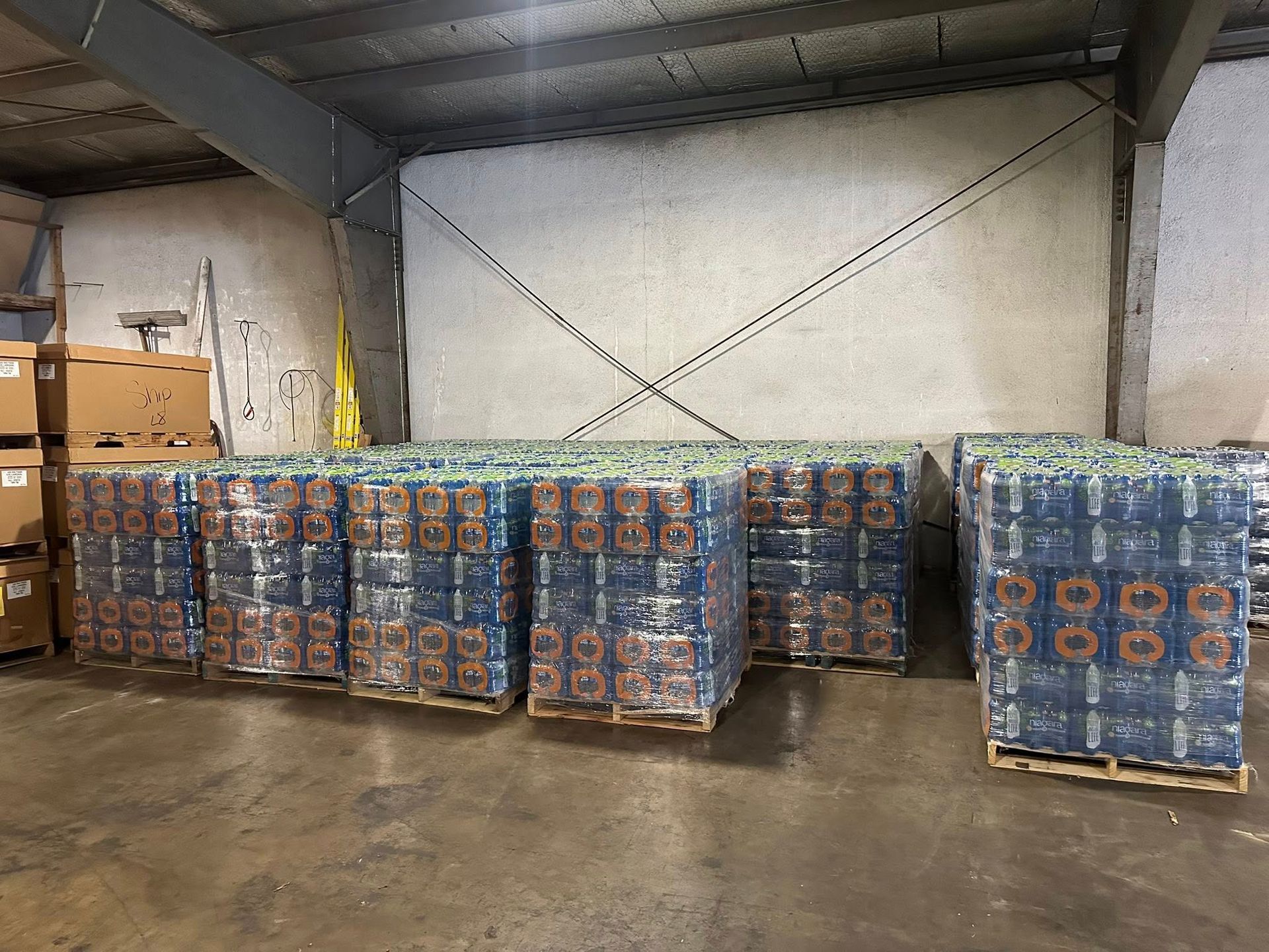 Pallets of bottled water wrapped in clear plastic in a warehouse setting.