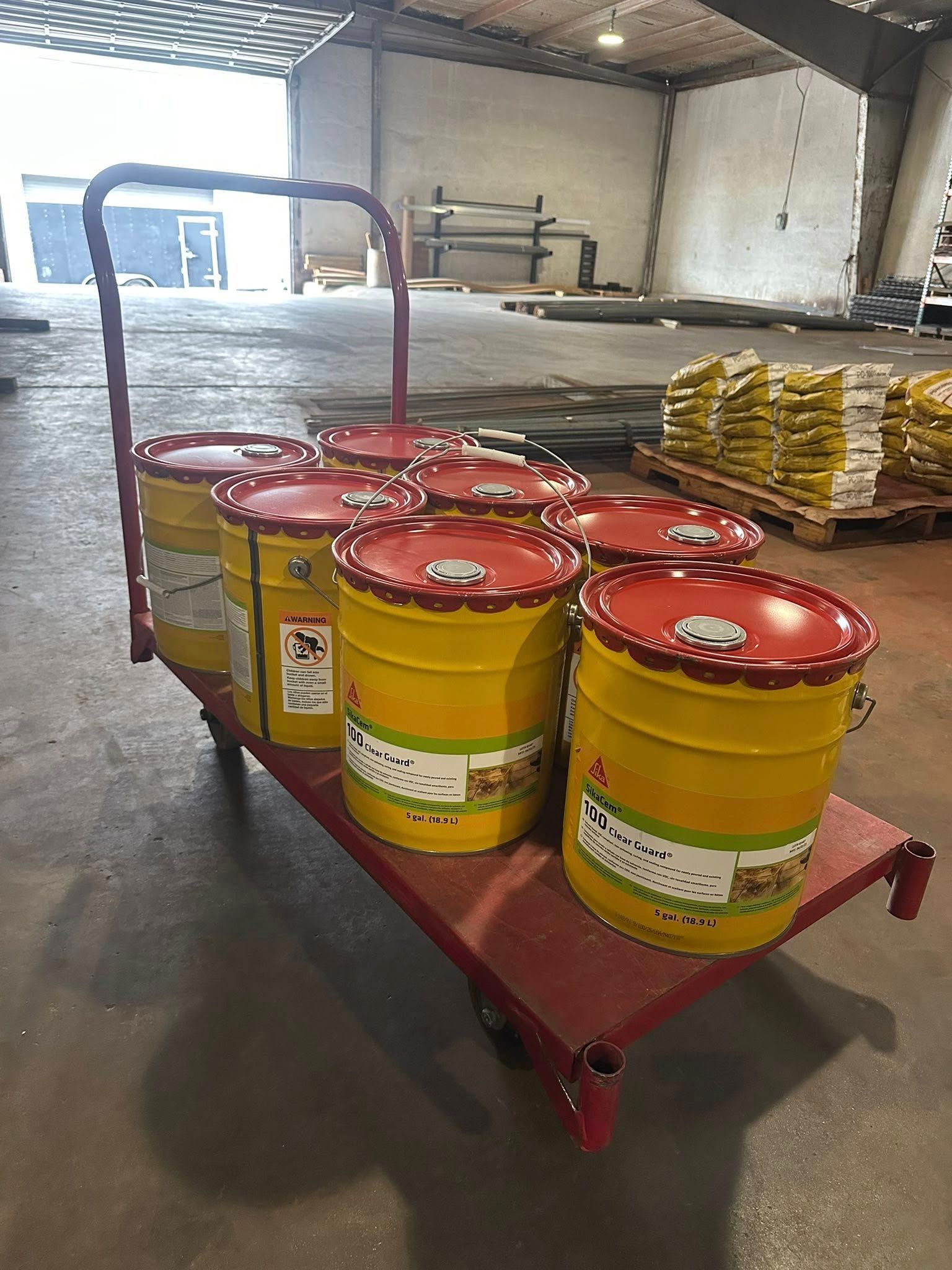 A red hand truck holding several yellow paint buckets with red lids inside a warehouse.