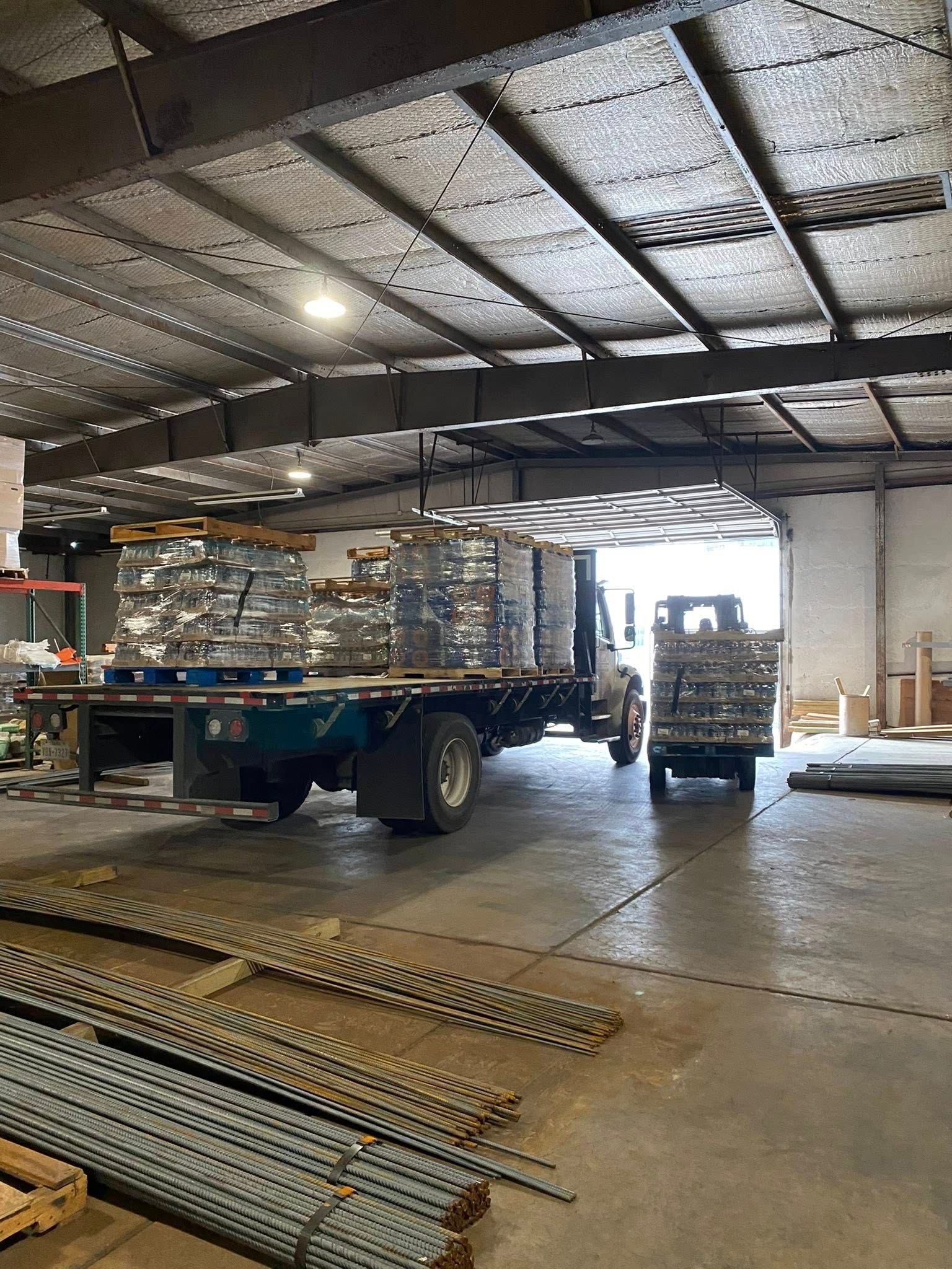 A flatbed truck loading pallets of materials inside a warehouse. Another cart with materials in foreground.