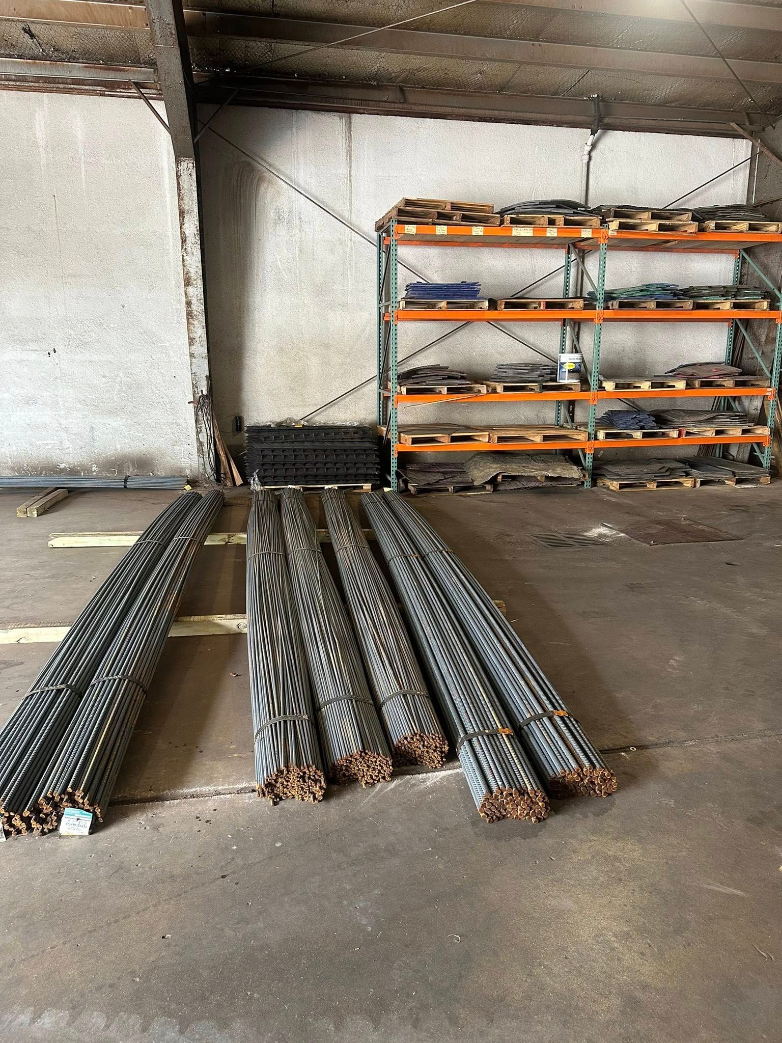 Bundles of rebar on a concrete floor in a warehouse. Shelves of materials are in the background.