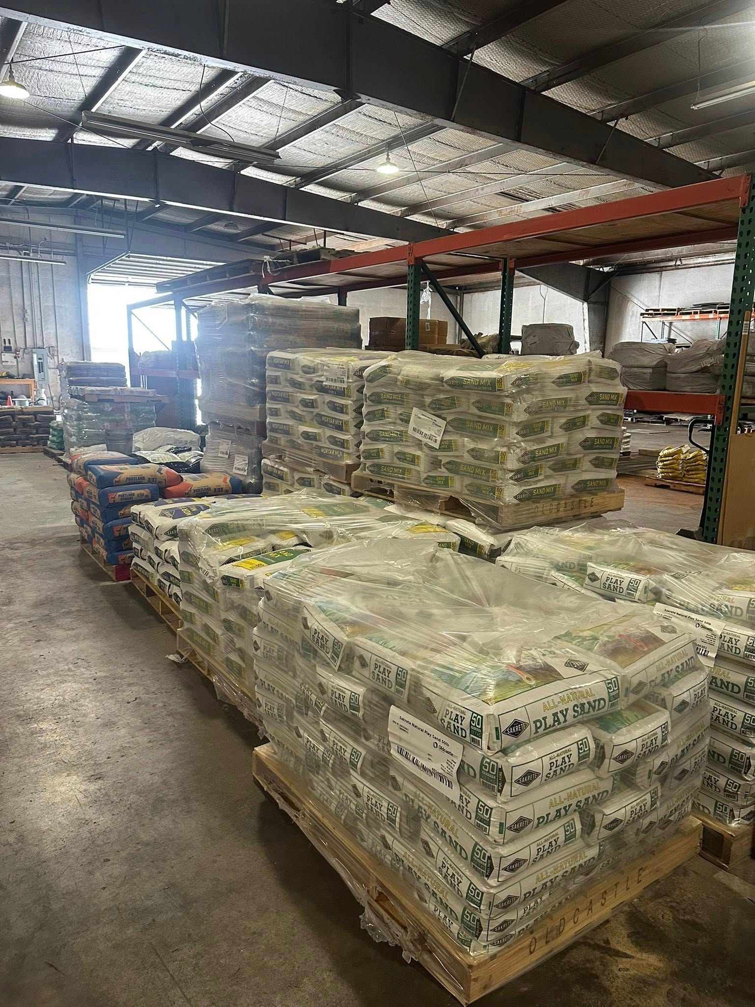 Warehouse interior with pallets of wrapped goods stacked near shelves.