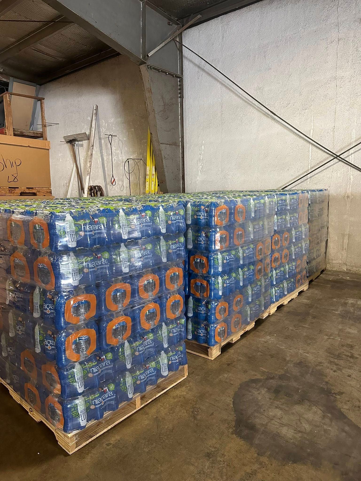 Pallets of bottled water wrapped in blue plastic inside a warehouse.