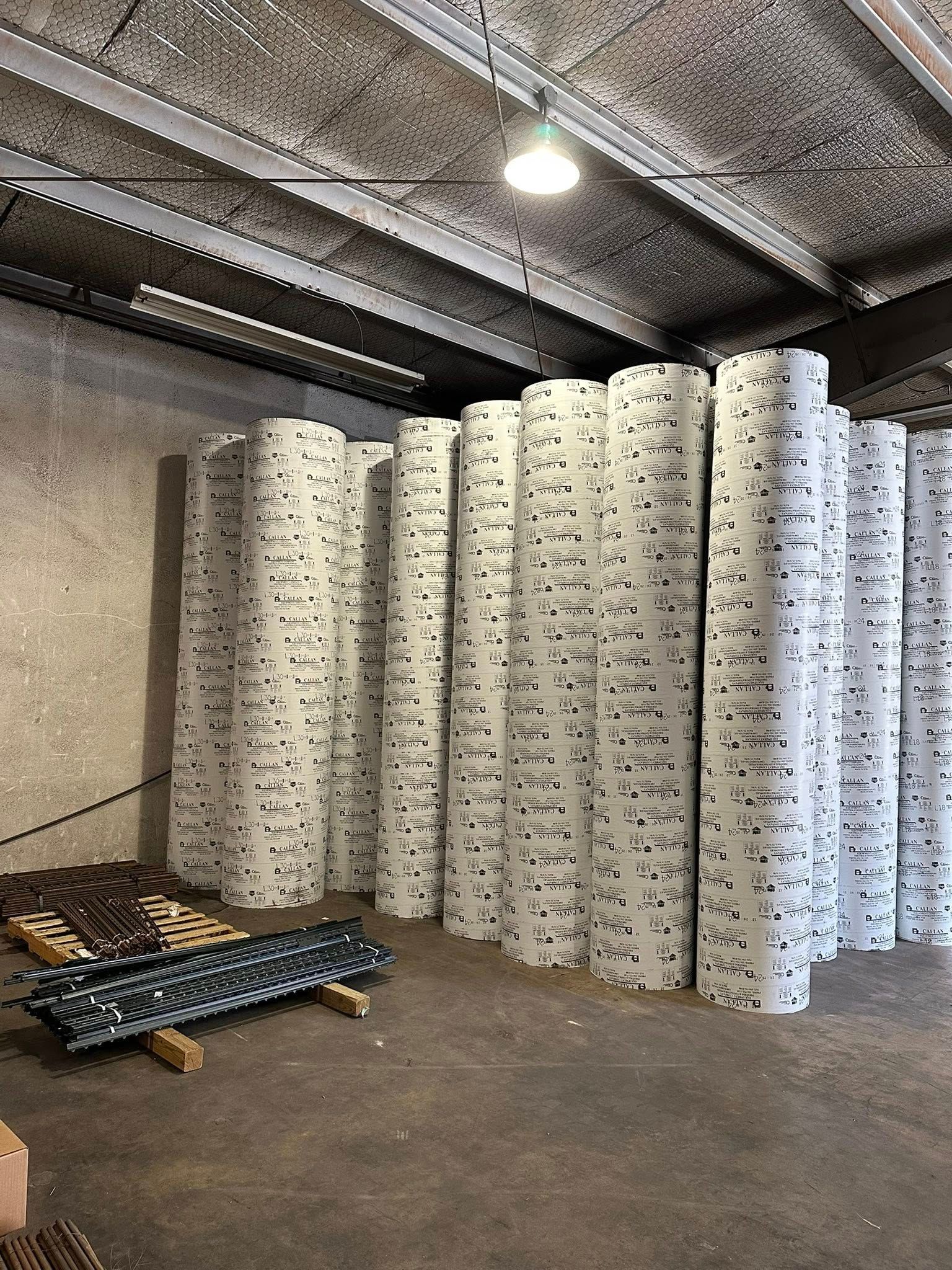 Rolls of white material stacked in a warehouse. A light hangs from the ceiling.