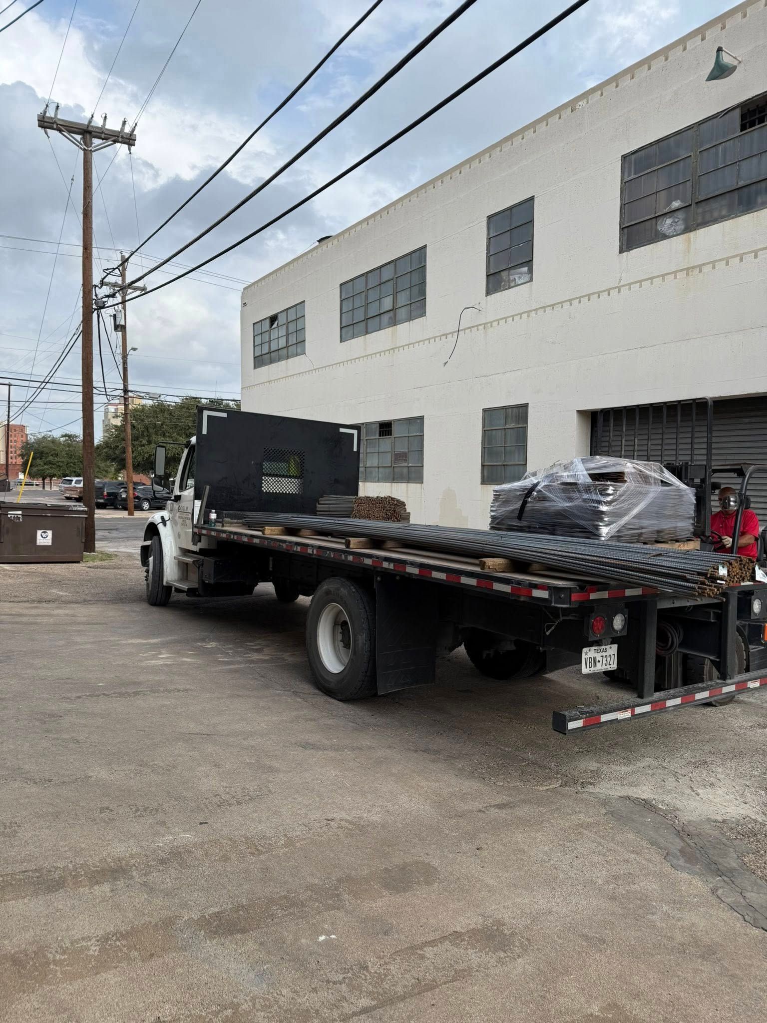 Flatbed truck loaded with dark materials near a white building with blacked-out windows.