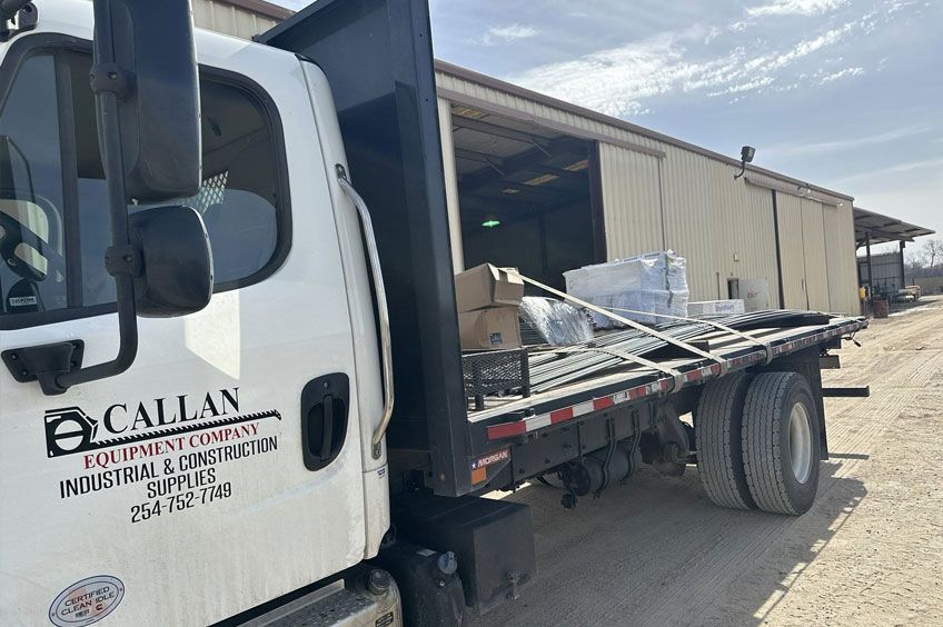 White truck with "Callan Equipment Company" logo parked next to a tan building; cargo on the flatbed.