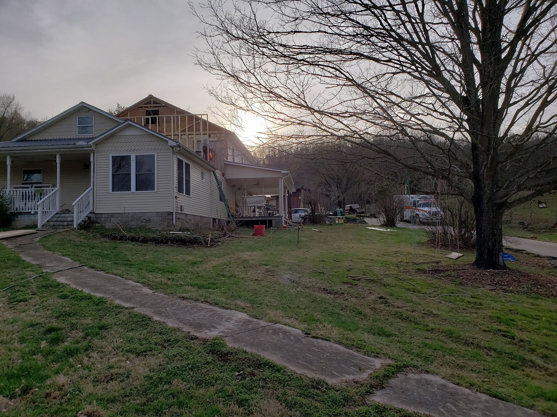 A house with a porch and unfinished construction during a cloudy sunset.
