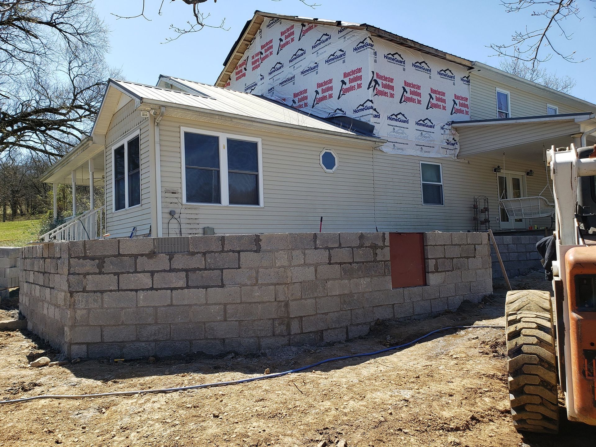 A two-story house with a stone wall in progress. Orange machinery is parked nearby.