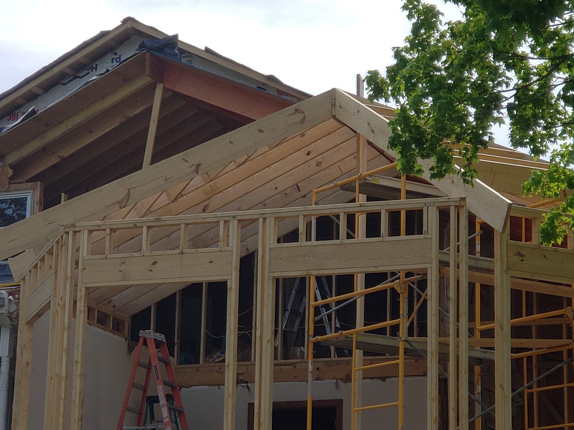 Wood frame of a building under construction with exposed beams and framing, a ladder, and scaffolding visible.
