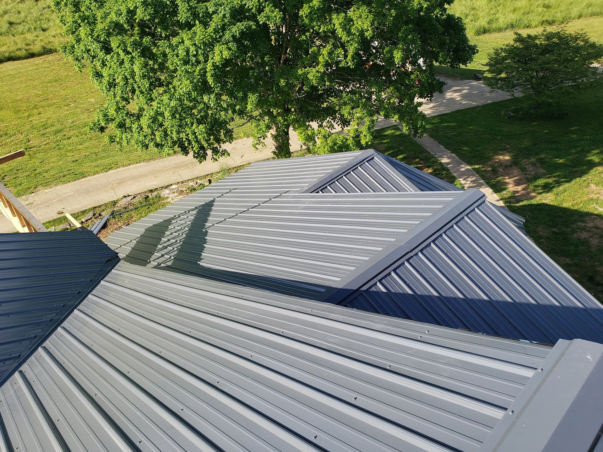 Gray metal roof with multiple angles, tree in background.