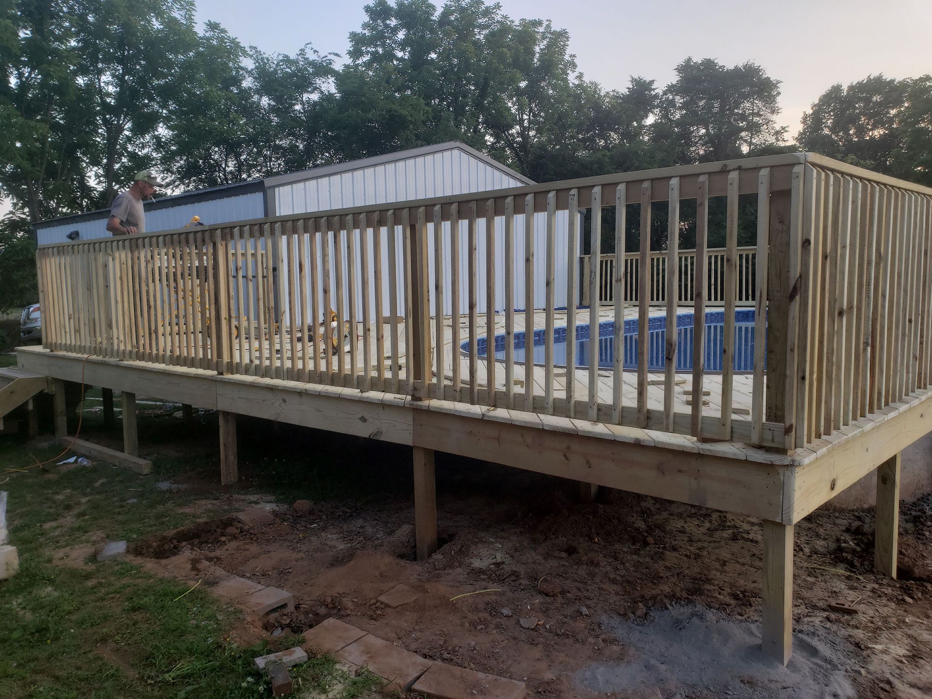 A newly built wooden deck surrounds an above-ground pool. A man stands on the deck.