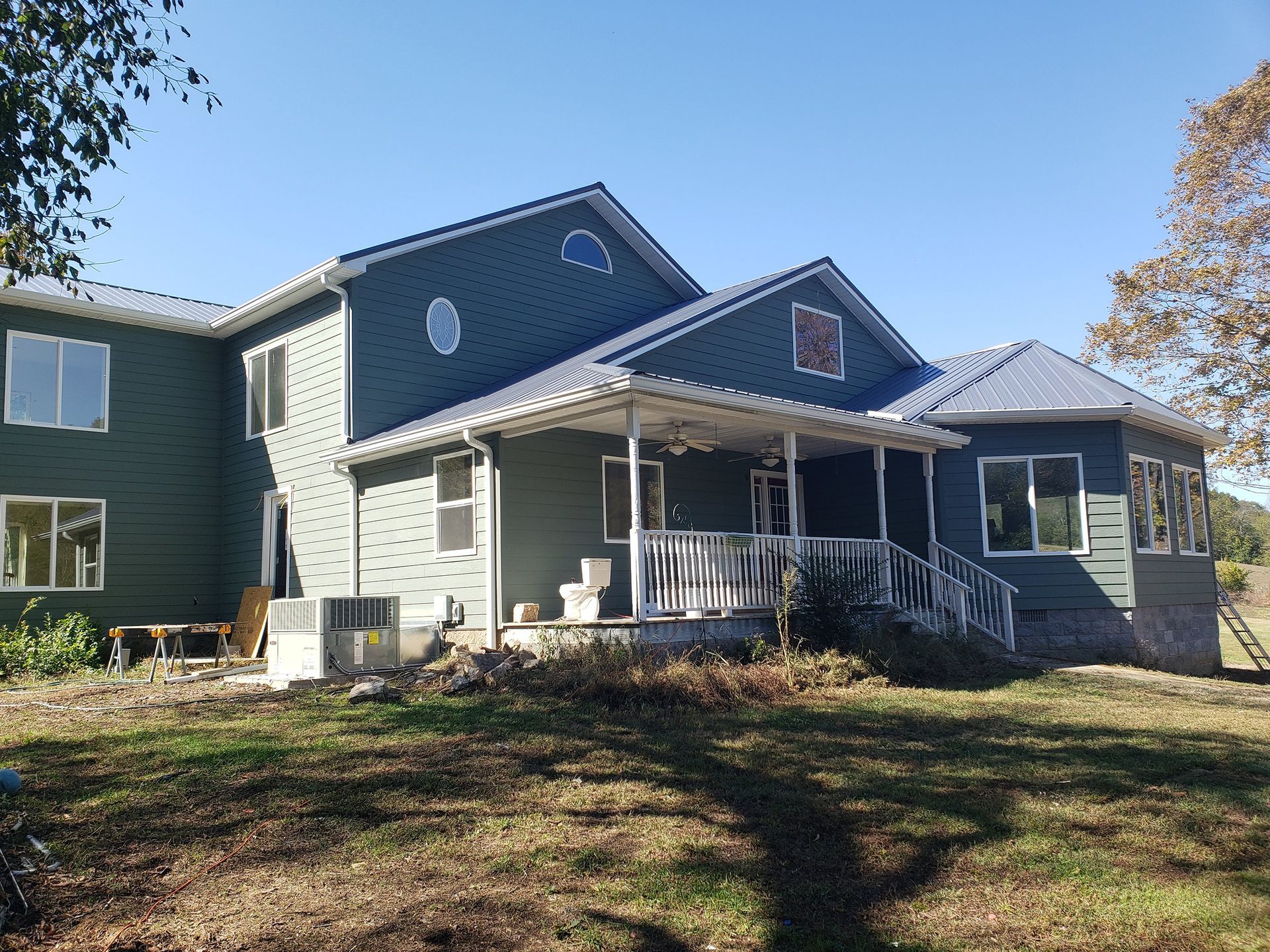 Green house with blue roof, porch and a clear sky in a rural area.