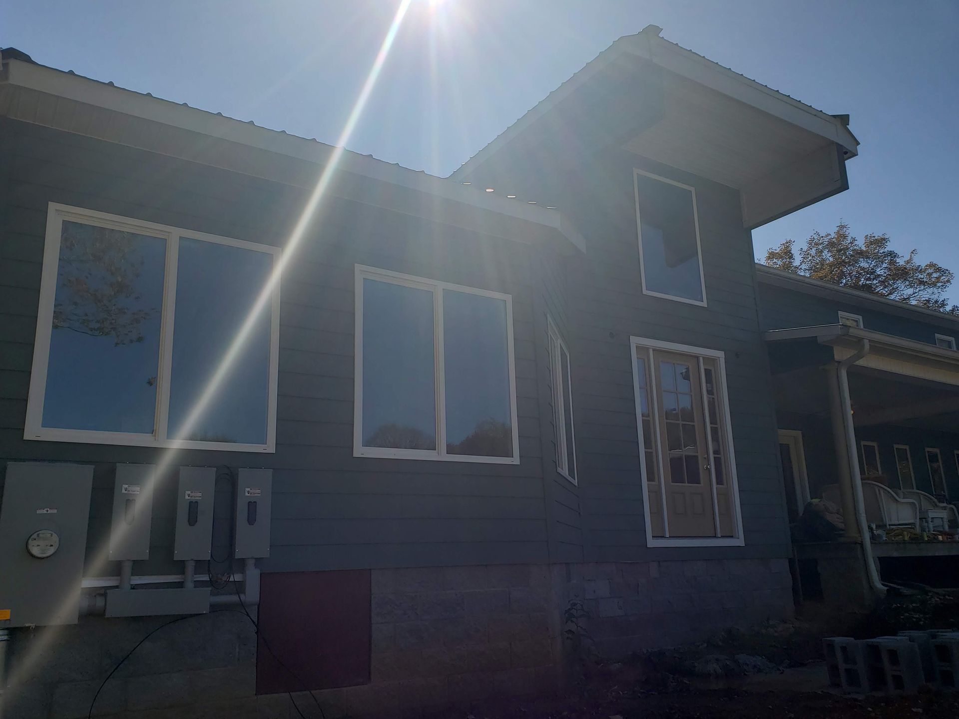 Gray house with white-framed windows, sun shining, electrical boxes.