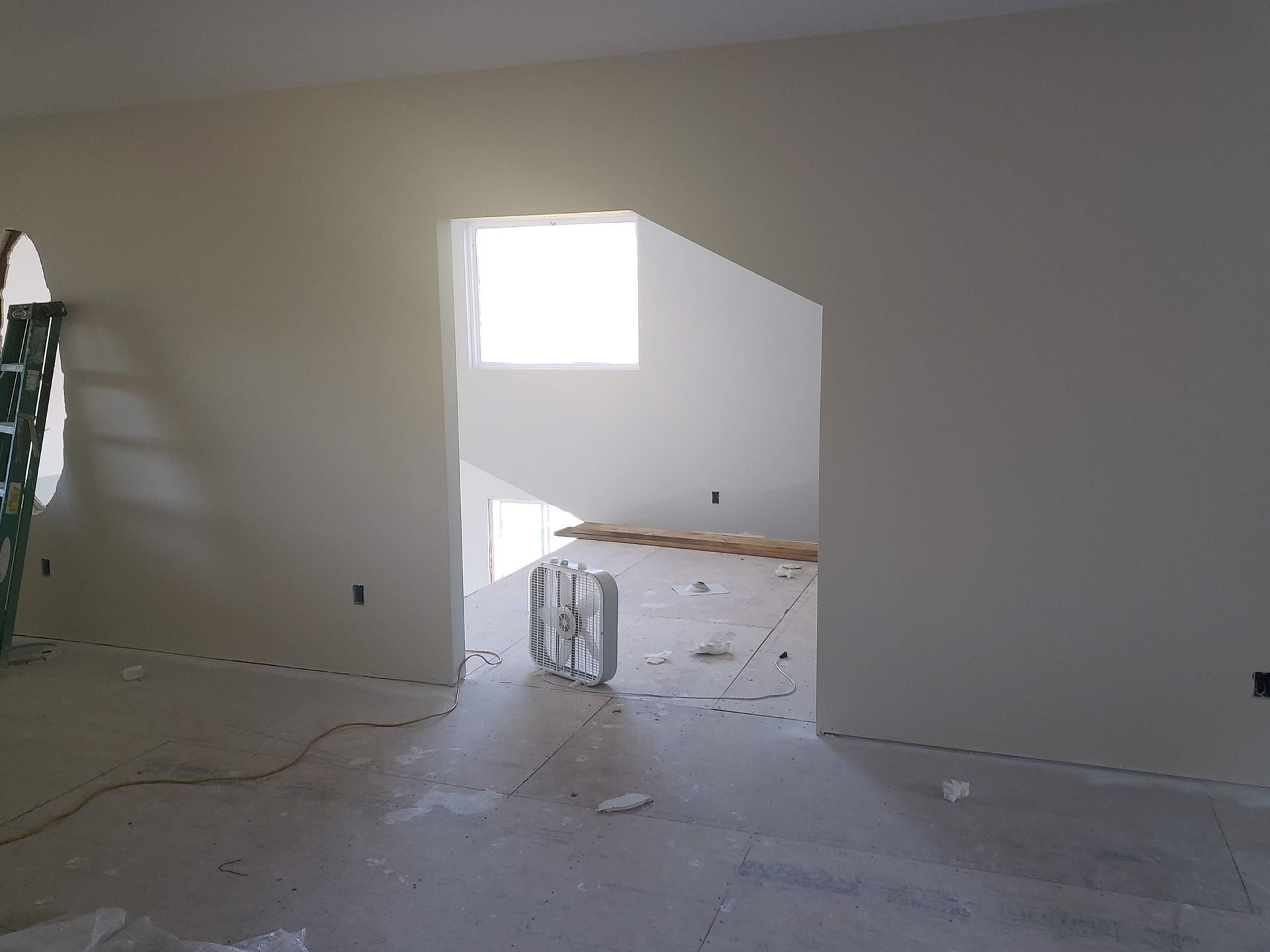 Interior of a room under construction, with an open doorway, light walls, and a bright window.